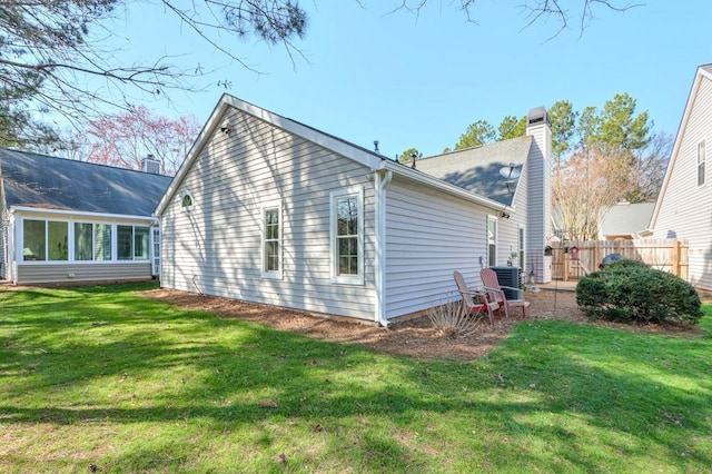 view of property exterior featuring a lawn, a chimney, central AC, and fence