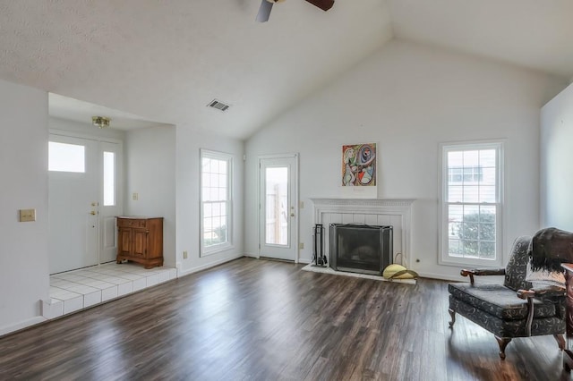 unfurnished living room featuring visible vents, dark wood-type flooring, high vaulted ceiling, and a tile fireplace