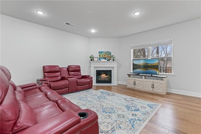 living room featuring light wood finished floors, visible vents, recessed lighting, and a glass covered fireplace