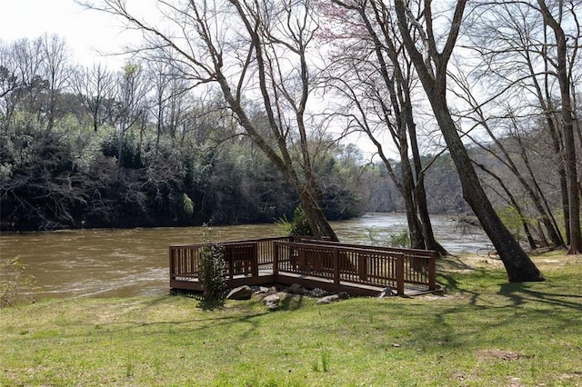 exterior space with a lawn, a view of trees, and a deck with water view