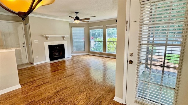 unfurnished living room with a textured ceiling, crown molding, a ceiling fan, and wood finished floors