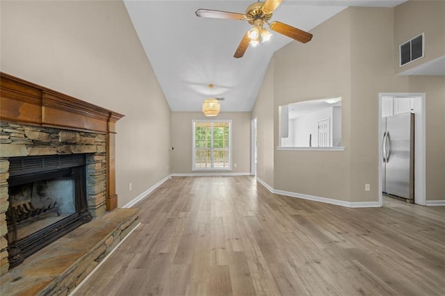 unfurnished living room featuring ceiling fan, a stone fireplace, light hardwood / wood-style flooring, and high vaulted ceiling