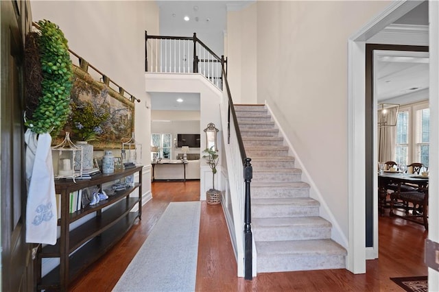 stairs featuring hardwood / wood-style floors, ornamental molding, and a high ceiling