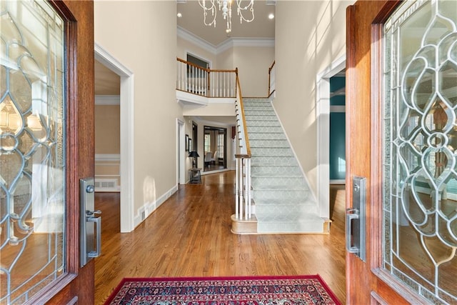 foyer entrance with ornamental molding, a chandelier, a towering ceiling, and hardwood / wood-style floors