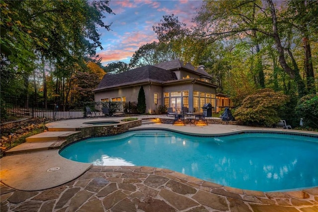 pool at dusk featuring an in ground hot tub and a patio area