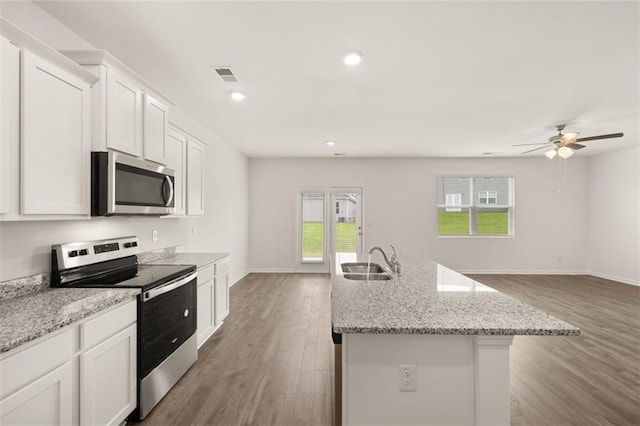 kitchen with light stone counters, stainless steel appliances, a kitchen island with sink, hardwood / wood-style flooring, and white cabinetry