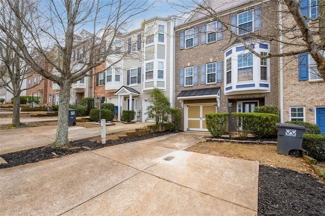 townhome / multi-family property with concrete driveway, a garage, brick siding, and a residential view