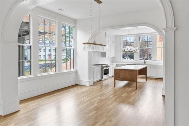 kitchen featuring high end stainless steel range, a kitchen island, white cabinetry, light hardwood / wood-style floors, and hanging light fixtures