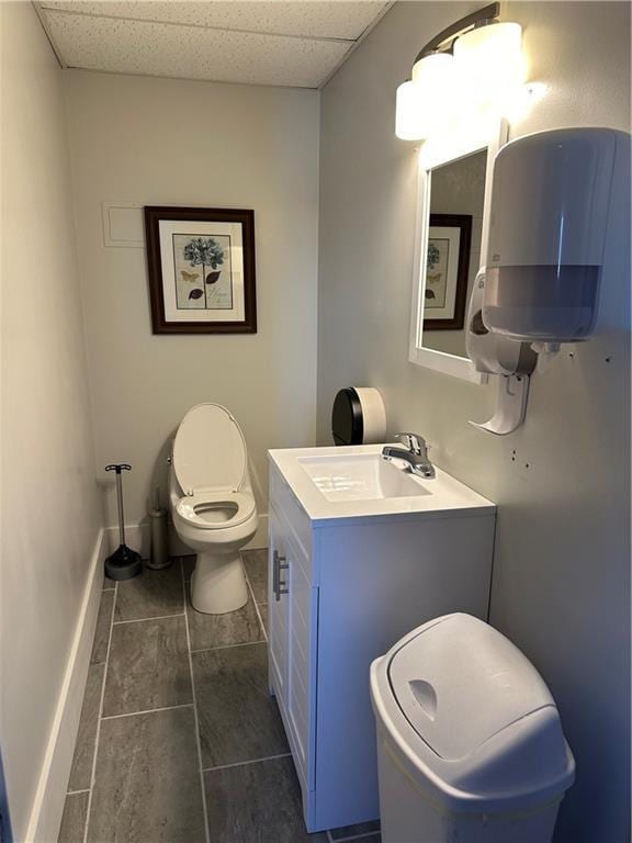 half bathroom with a paneled ceiling, tile patterned floors, baseboards, vanity, and toilet