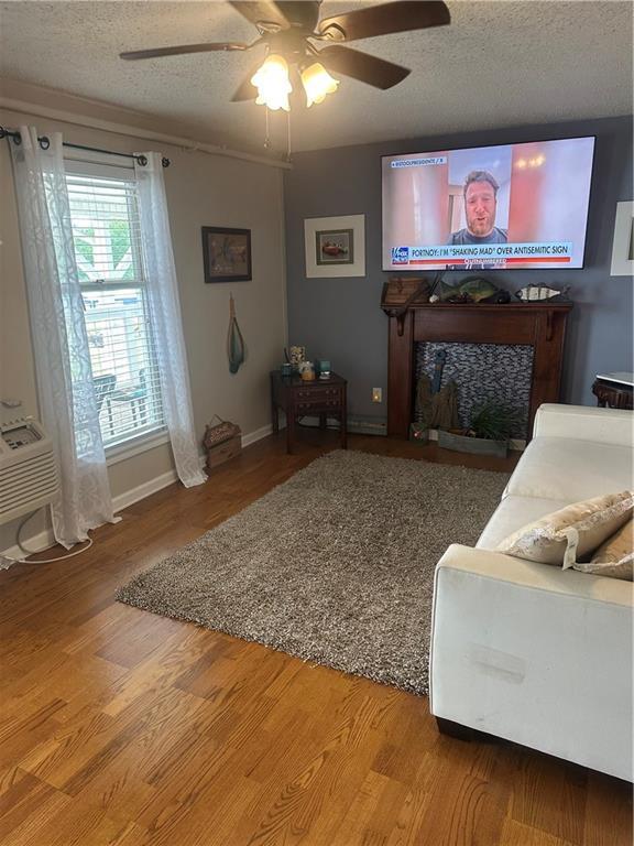 living room with ceiling fan, a textured ceiling, baseboards, and light wood-type flooring