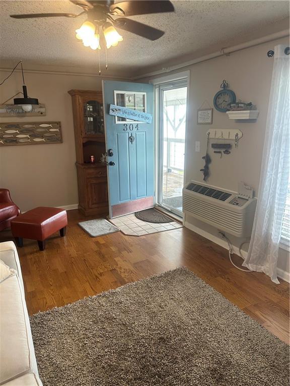 foyer entrance with a wall unit AC, ceiling fan, a textured ceiling, and wood finished floors