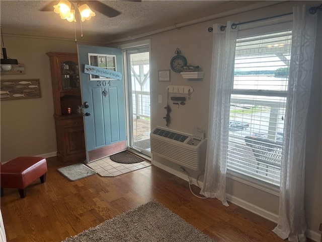 foyer entrance with a wall mounted AC, a textured ceiling, wood finished floors, and ceiling fan