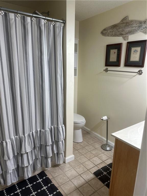 full bath with toilet, a shower with shower curtain, tile patterned floors, baseboards, and vanity