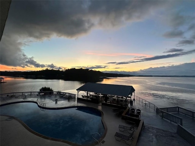 pool at dusk with a community pool and a water view