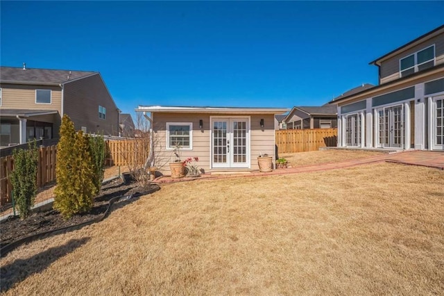 rear view of property featuring an outbuilding, a yard, french doors, and a fenced backyard