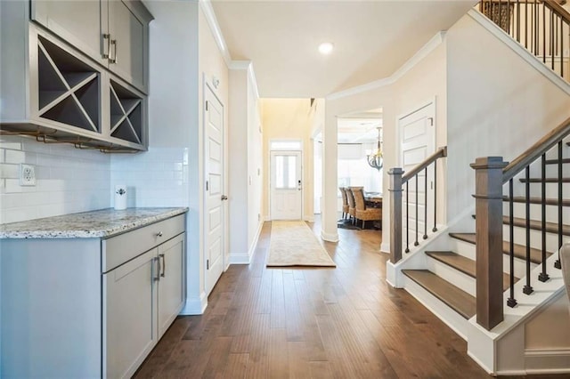 foyer featuring stairway, an inviting chandelier, dark wood-type flooring, ornamental molding, and baseboards