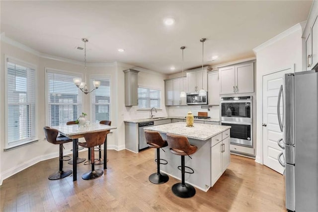 kitchen featuring wood finished floors, a kitchen island, a sink, appliances with stainless steel finishes, and crown molding