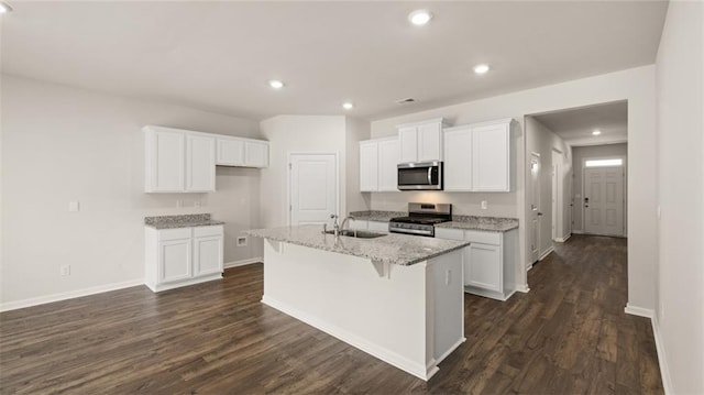 kitchen with appliances with stainless steel finishes, dark hardwood / wood-style flooring, white cabinetry, and an island with sink