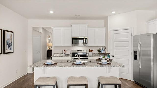 kitchen featuring dark wood-type flooring, stainless steel appliances, a center island with sink, and white cabinets