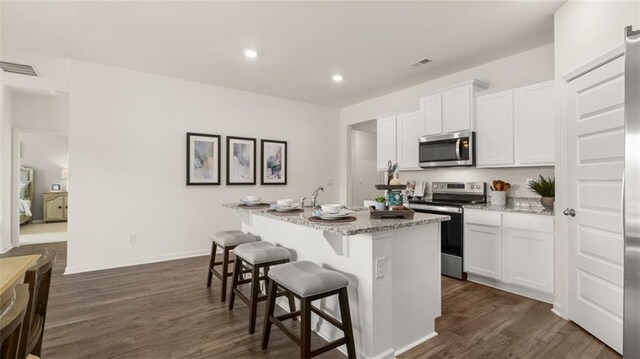 kitchen with white cabinetry, a kitchen bar, stainless steel appliances, an island with sink, and dark wood-type flooring