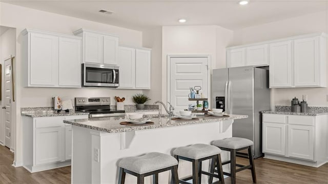 kitchen with an island with sink, stainless steel appliances, wood-type flooring, and white cabinets