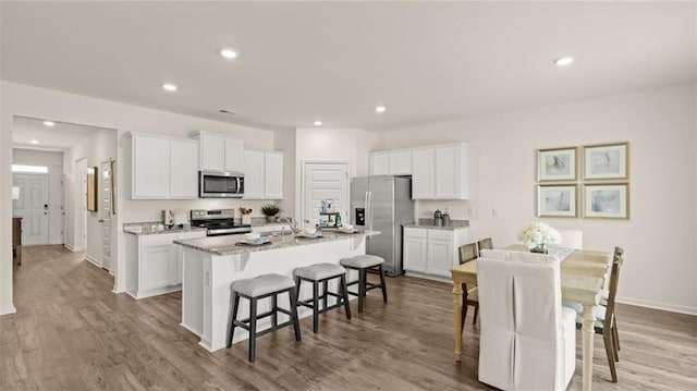 kitchen with a breakfast bar area, stainless steel appliances, an island with sink, and white cabinetry