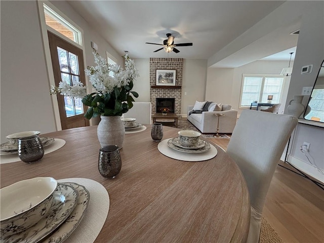 living room with a brick fireplace, ceiling fan, and wood finished floors