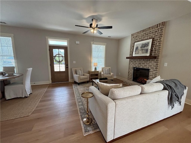 living room featuring a fireplace, wood finished floors, a ceiling fan, and baseboards