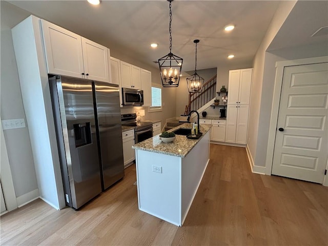 kitchen with stainless steel appliances, light wood-style floors, white cabinets, a sink, and light stone countertops