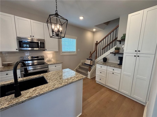 kitchen with light stone counters, white cabinetry, light wood-style floors, appliances with stainless steel finishes, and pendant lighting