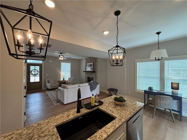 kitchen featuring a sink, visible vents, stainless steel dishwasher, a brick fireplace, and pendant lighting