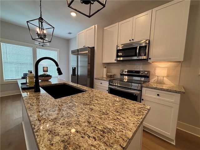 kitchen with stainless steel appliances, wood finished floors, a sink, white cabinetry, and decorative backsplash