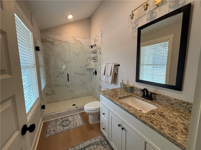 bathroom with a marble finish shower, toilet, wood finished floors, vaulted ceiling, and vanity