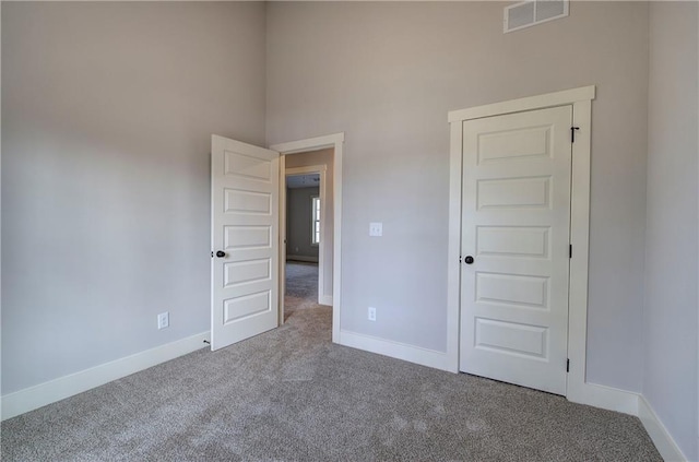 spare room featuring a high ceiling, carpet, visible vents, and baseboards