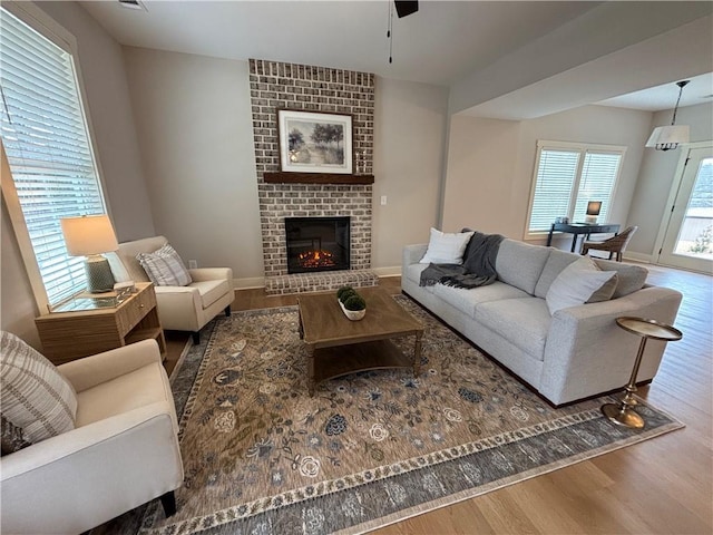 living room with a brick fireplace, a wall unit AC, baseboards, and wood finished floors