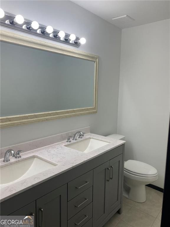 bathroom with double vanity, tile patterned flooring, toilet, and a sink