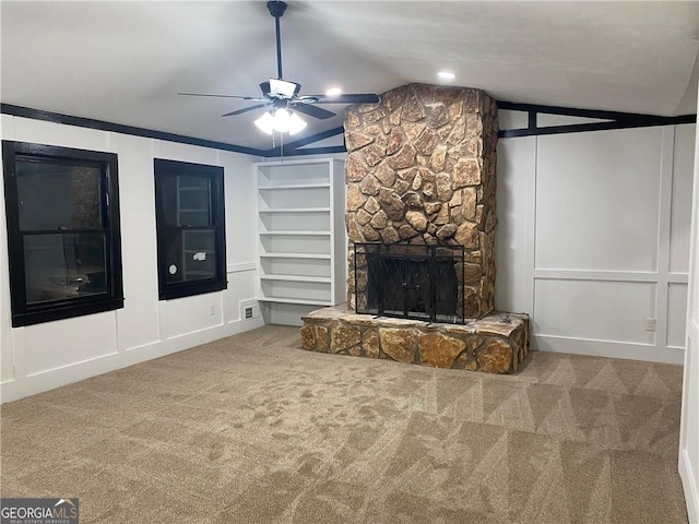 unfurnished living room featuring a fireplace, ceiling fan, vaulted ceiling, a decorative wall, and carpet flooring