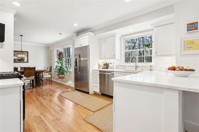 kitchen with sink, white cabinets, hanging light fixtures, ornamental molding, and stainless steel appliances