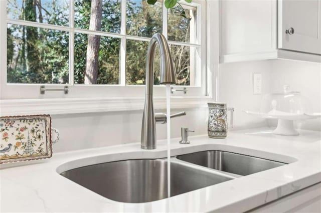 room details featuring white cabinetry, sink, and light stone counters