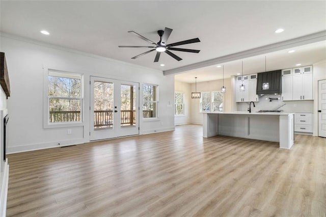 unfurnished living room featuring ceiling fan, sink, crown molding, and light wood-type flooring