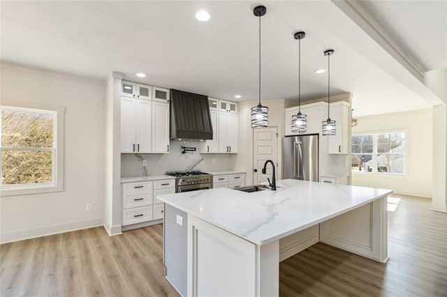 kitchen featuring decorative light fixtures, premium range hood, sink, an island with sink, and stainless steel appliances