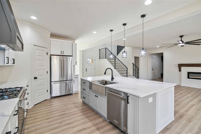 kitchen featuring stainless steel appliances, an island with sink, ceiling fan, sink, and light stone counters