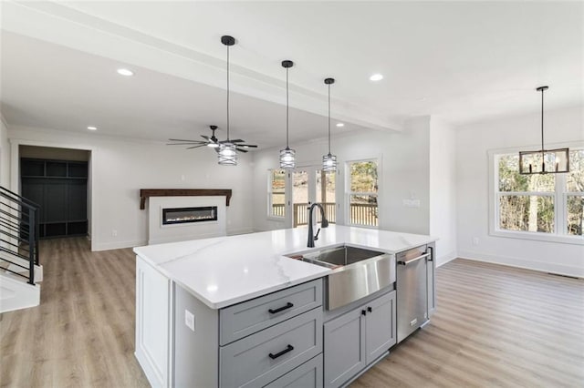 kitchen featuring pendant lighting, sink, gray cabinets, a kitchen island with sink, and stainless steel dishwasher