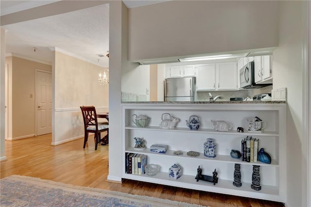 kitchen featuring white cabinetry, an inviting chandelier, wood-type flooring, stainless steel appliances, and light stone countertops