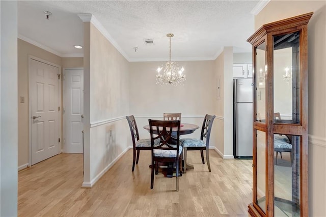 dining space featuring ornamental molding, an inviting chandelier, a textured ceiling, and light wood-type flooring