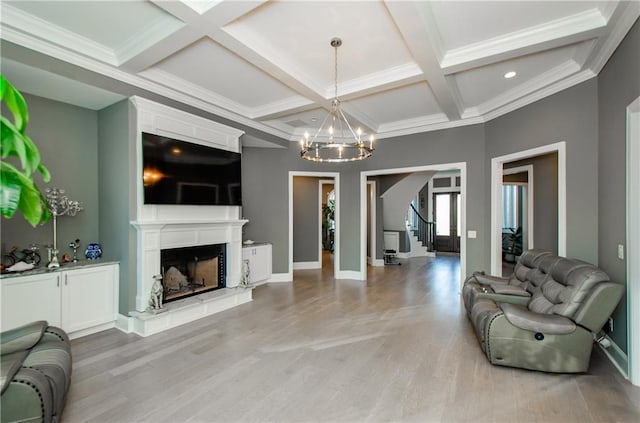 living room featuring a fireplace with raised hearth, light wood-style floors, a chandelier, coffered ceiling, and beamed ceiling