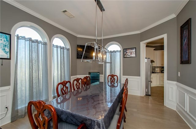 dining area featuring an inviting chandelier, crown molding, light hardwood / wood-style floors, and a wealth of natural light