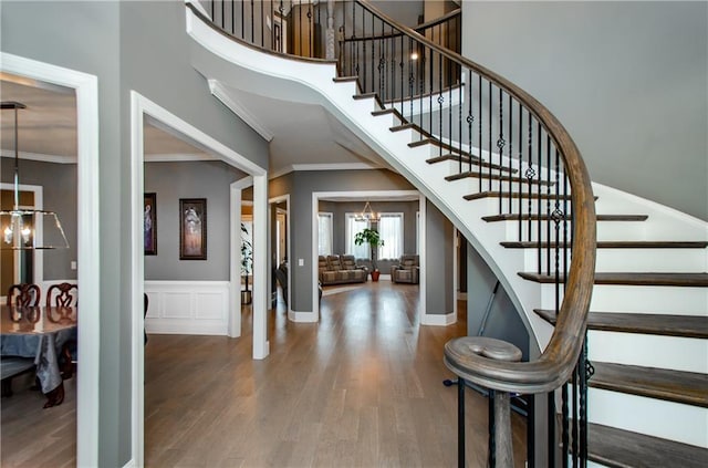 stairway featuring wainscoting, ornamental molding, wood finished floors, a high ceiling, and a chandelier