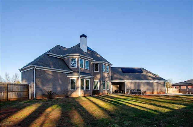 back of property featuring a chimney, fence, a lawn, and brick siding