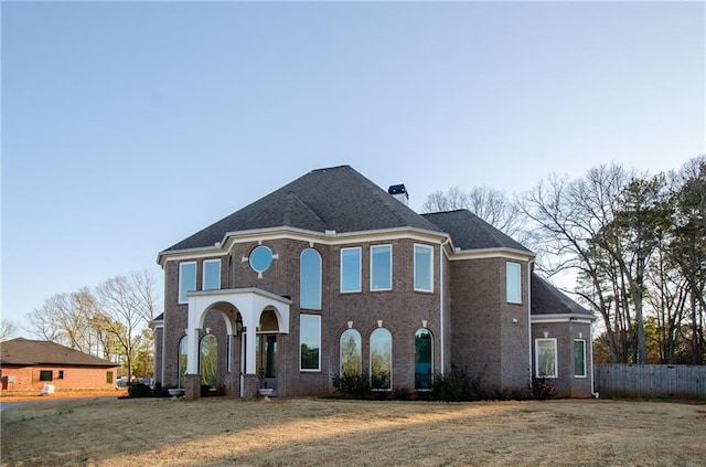 view of front facade with brick siding, a chimney, a front lawn, and fence